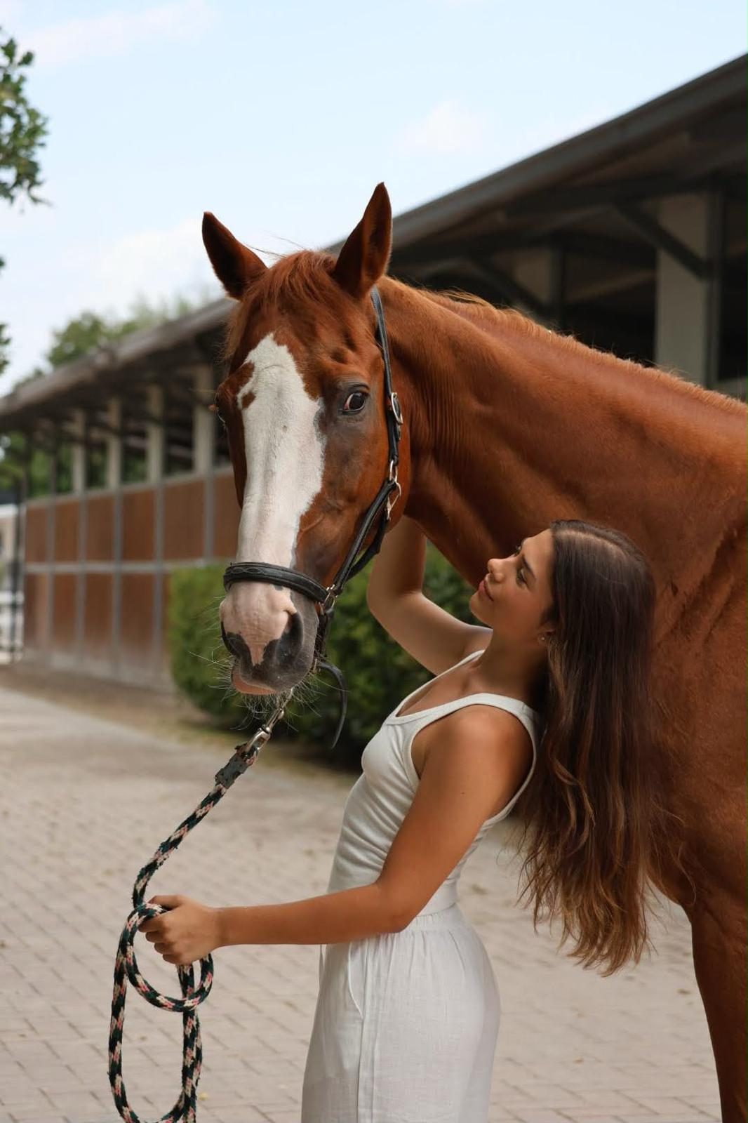 Ragazza accanto a un cavallo sauro davanti alle scuderie
