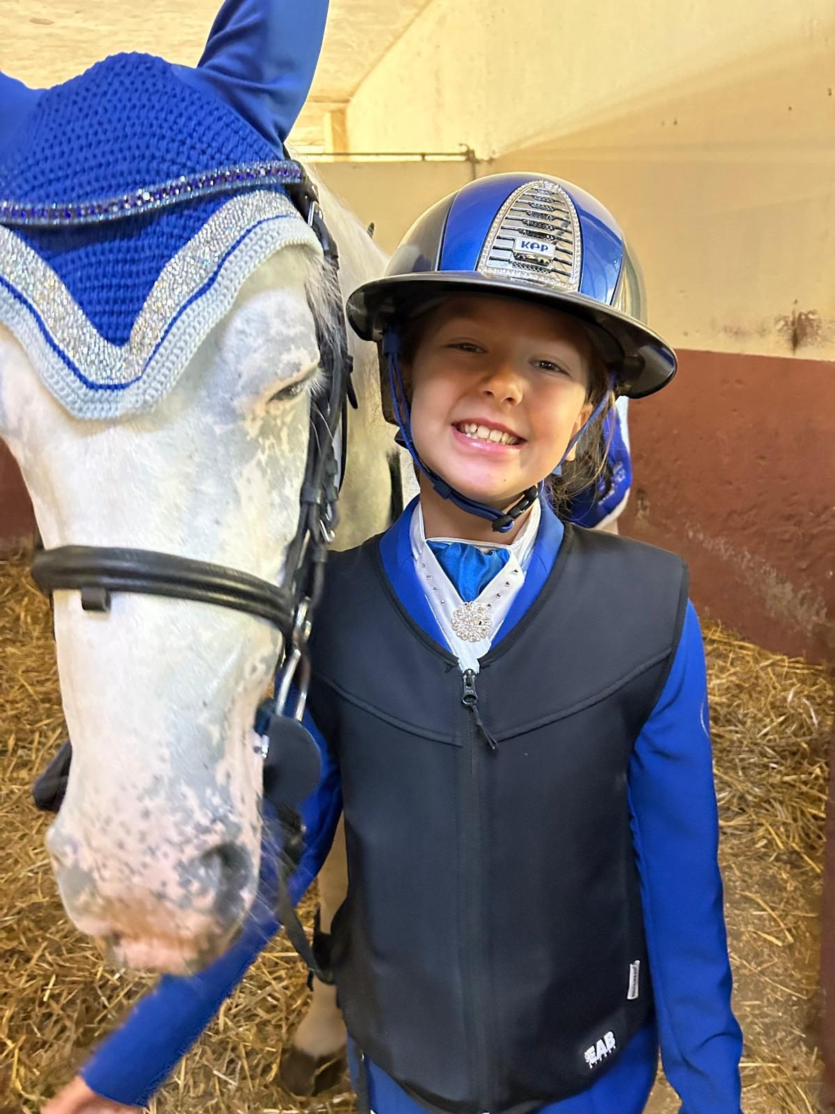 Giovane allieva sorridente accanto al suo pony nella scuderia